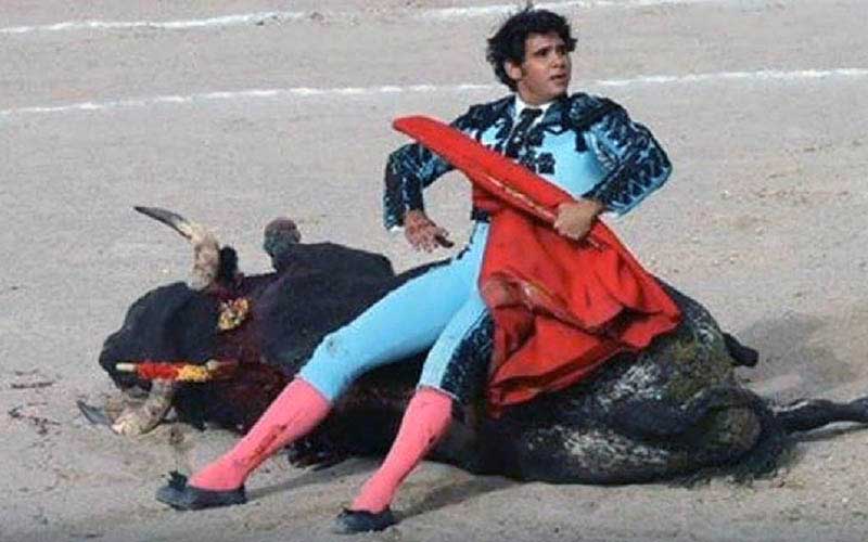 Un matador assis sur un taureau mort dans l'arène, tenant sa muleta.