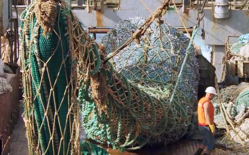 Une vue plus large du pont d'un navire où l'on manipule de grands filets et équipements de pêche.
